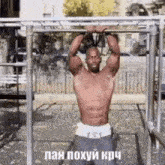 a shirtless man is doing pull ups on a bar with russian writing on it .