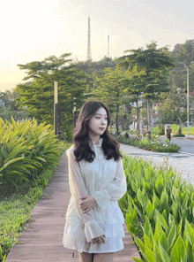 a woman in a white dress stands on a wooden path