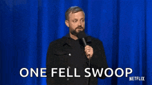 a man with a beard is standing in front of a microphone and saying one fell swoop .