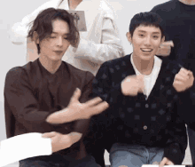 two men are sitting next to each other and one is wearing a black cardigan