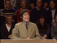 a man in a suit is laughing in front of a crowd of people