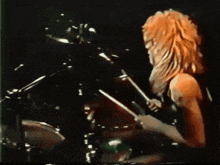 a man with green hair is playing drums in a dark room with green lights behind him