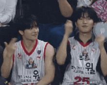 a couple of basketball players are sitting in the stands with their hands in the air .