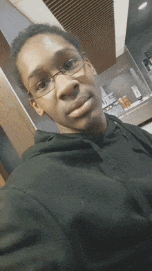 a young man wearing glasses and a black hoodie is taking a selfie