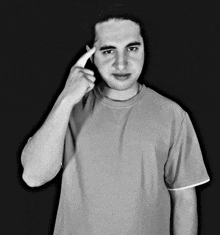 a man in a grey shirt is pointing at his head