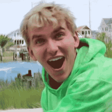 a young man in a green hoodie is smiling with his mouth open