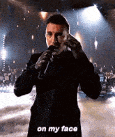 a man in a suit is singing into a microphone on a stage and says `` on my face '' .