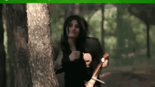 a woman is standing next to a tree in the woods