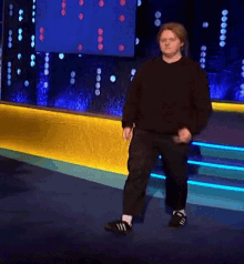 a man in a black sweater and black pants is dancing on a stage
