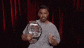 a man is holding a wrestling championship belt in front of a red curtain on a stage .