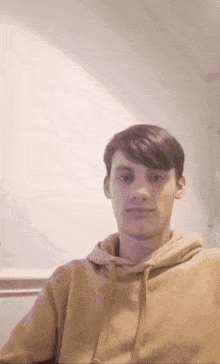 a young man is wearing a tan hoodie and looking at the camera