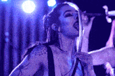 a woman with a tattoo of a spider on her arm sings into a microphone