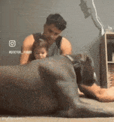 a man and a child are playing with a large dog on the floor .