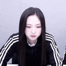 a woman wearing a black jacket with white stripes on the sleeves looks down