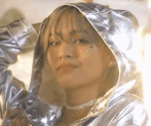 a woman wearing a silver jacket with a hood and a choker is looking at the camera .