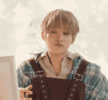 a young man in plaid overalls is holding a brush and looking at a picture .