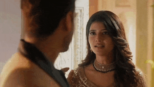 a man and a woman are looking at each other in a room . the woman is wearing a necklace .
