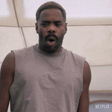 a man in a grey tank top is standing in front of a sign for netflix