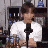 a man in a white shirt is sitting in front of a microphone with bottles of beer in the background .