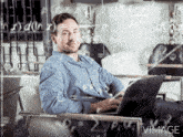 a man sits in a chair with a laptop in front of a glass wall with mathematical equations on it