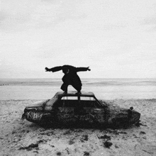 a black and white photo of a man standing on top of a car that has graffiti on it