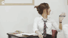 a girl in a school uniform is sitting at a desk in a classroom with another girl .