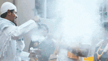 a man in a white hat is stirring a pot of food with smoke coming out of it