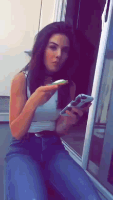 a woman in a white tank top is holding a remote control