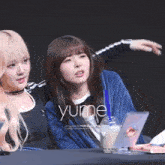 two girls are sitting at a table and the word yume is on the bottom right