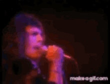 a woman is singing into a microphone in a dark room with purple lights behind her .