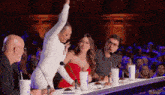 a woman in a white dress is standing in front of a microphone while a group of people sit at a table .