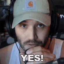 a man wearing headphones and a carhartt hat is saying yes