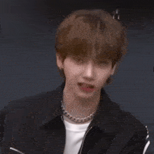 a young man wearing a black jacket and a necklace