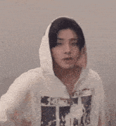 a young man wearing a white hoodie is covering his mouth with his hand .