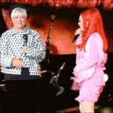 a woman in a pink dress stands next to a woman in a black and white jacket holding a microphone