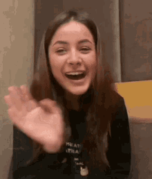 a woman is laughing and waving her hand at the camera .
