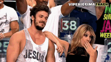 a man wearing a tank top that says jesus is standing next to a woman