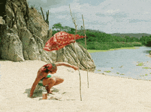 a man squatting on a beach with a bottle of soda in his hand