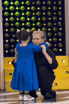 a little girl in a blue dress hugging a man
