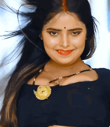 a woman wearing a black top and a gold necklace is smiling