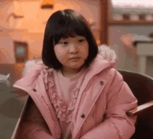 a little girl in a pink jacket is sitting in a chair .