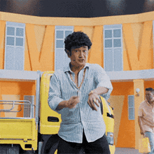 a man in a striped shirt is standing in front of a yellow truck