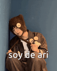 a man wearing a hat and holding a teddy bear with the words soy de ari written on the bottom