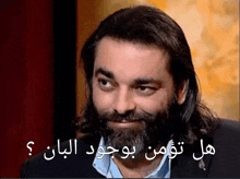 a man with long hair and a beard is smiling with arabic writing on the bottom