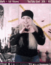 a woman is making a heart shape with her hands while wearing a black beanie