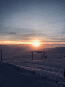 a sunset over a snowy mountain with a ski lift in the background