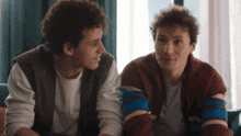 two young men are sitting next to each other looking at each other