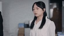 a woman in a white shirt is standing in an office with her eyes closed