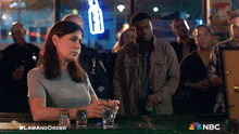 a woman sits at a bar holding a shot glass with nbc written on the bottom right