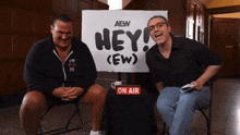 two men sitting in front of a sign that says hey ( ew )